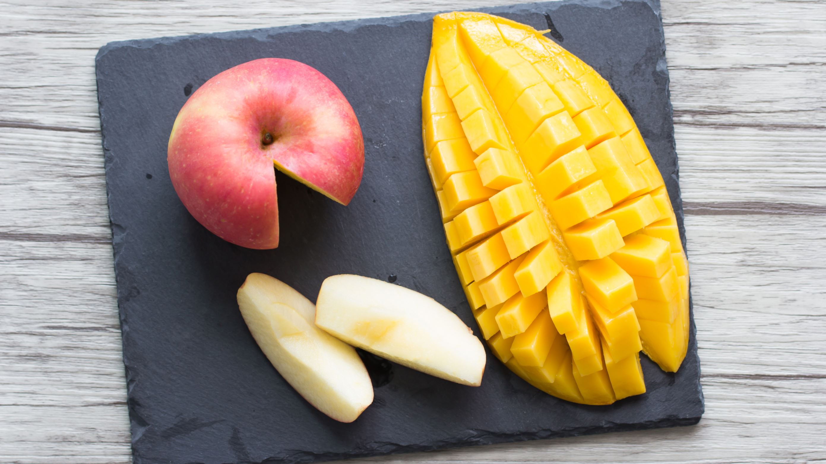 Mango and apple on a black stone plate