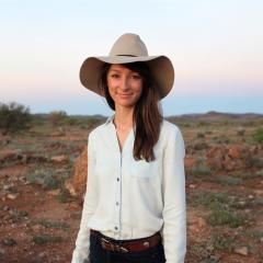 Headshot of Dr Anika Molesworth standing in a stark rural setting with sun setting behind 