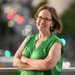 Headshot of Prof Heather Smyth with arms crossed and city lights in background