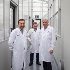 Three men in white coats standing in a windowed hallway