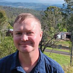 PhD candidate Brandon Fraser standing in a rural setting with paddocks stretching behind him