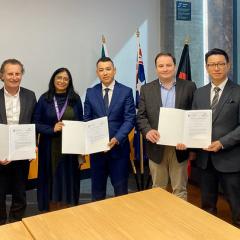 seven people holding signed mou around boardroom table 